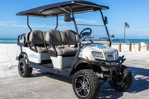 A white golf cart with six seats on the beach.